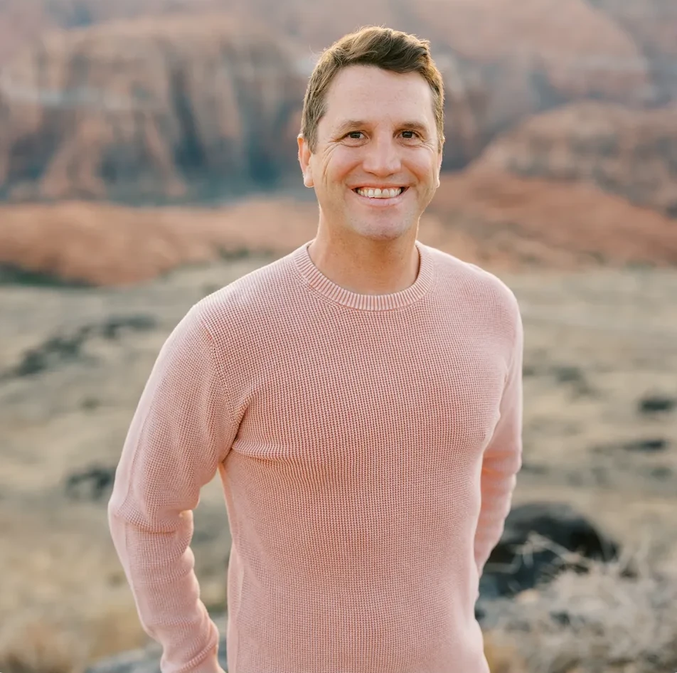 Matt Winkley smiles while standing on a rocky desert landscape outdoors.